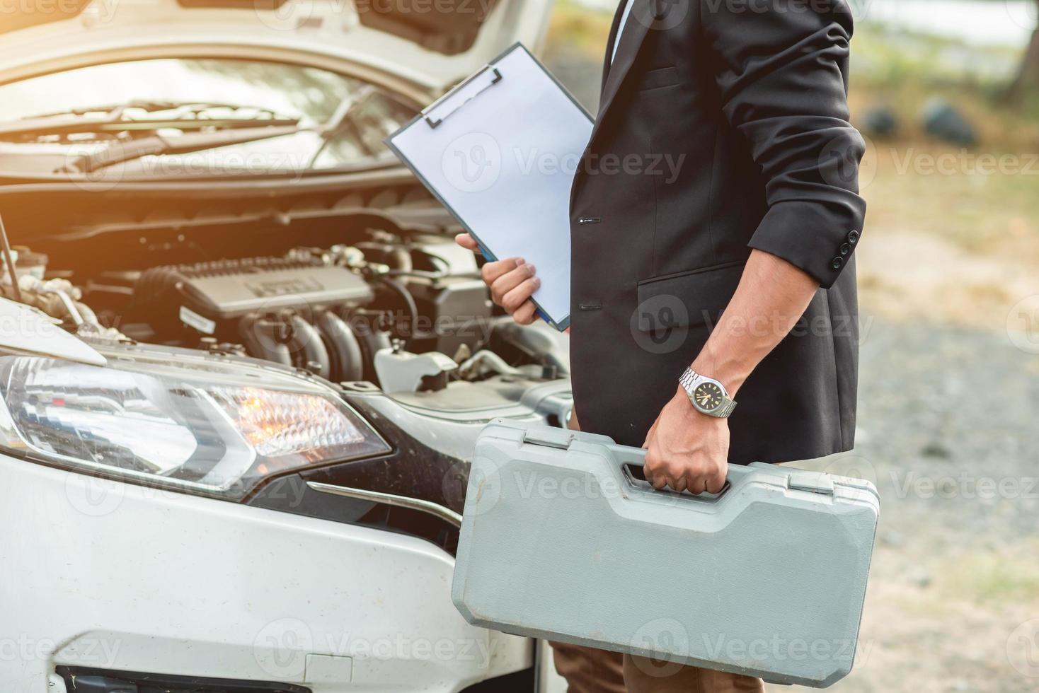 The auto mechanic is carrying the equipment to fix the car and has a repair log. photo