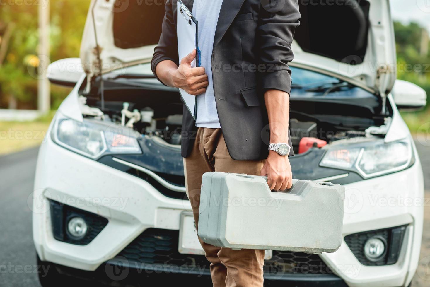 The auto mechanic is carrying the equipment to fix the car and has a repair log. photo