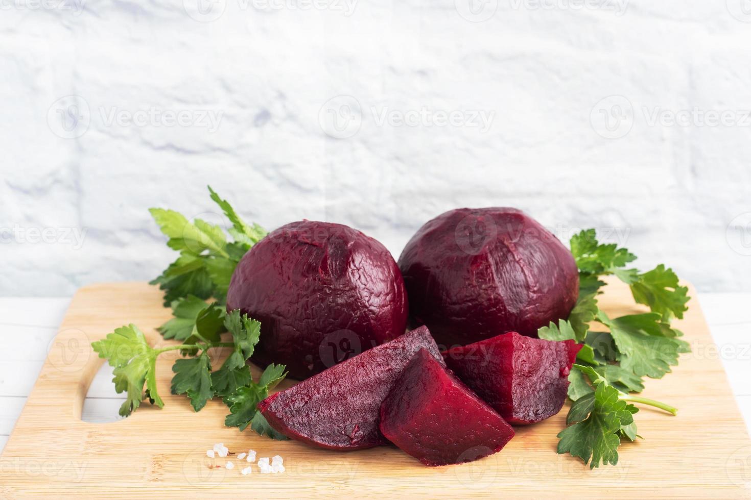 Boiled beets whole and cut on a cutting Board with parsley leaves on a white background. Copy space photo