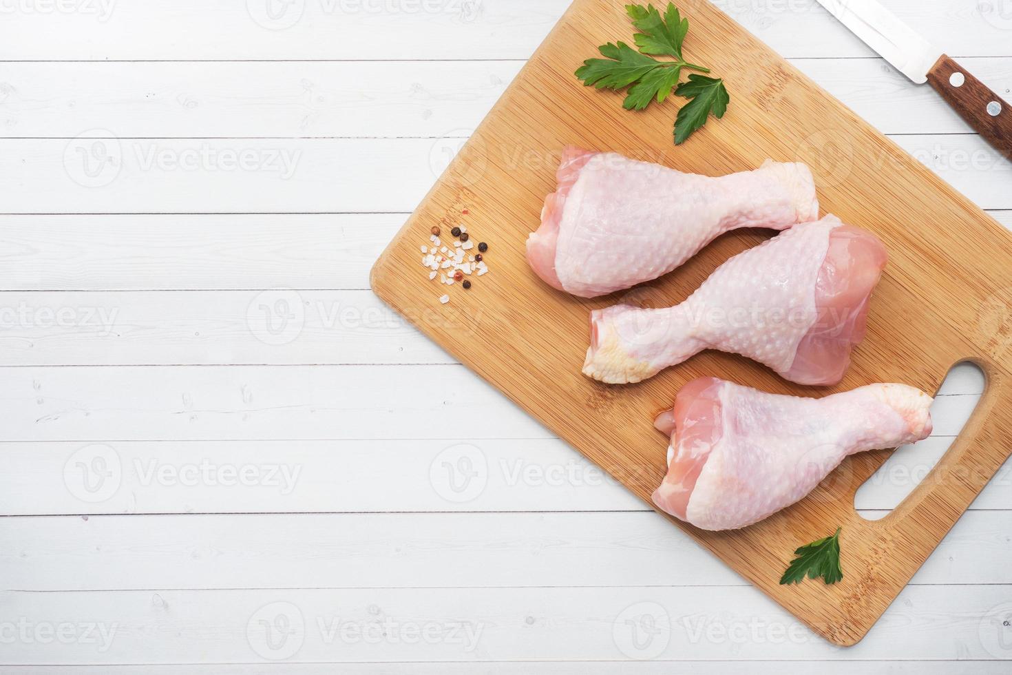 muslos de pollo crudo con perejil y especias en una tabla de cortar de madera. espacio de copia de vista superior foto