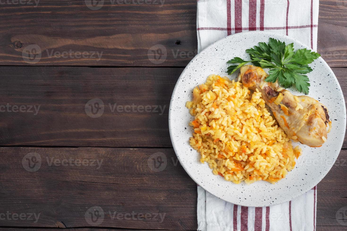 Delicious Asian pilaf, stewed rice with vegetables and chicken drumstick on a plate. Wooden rustic background. Copy space top view photo