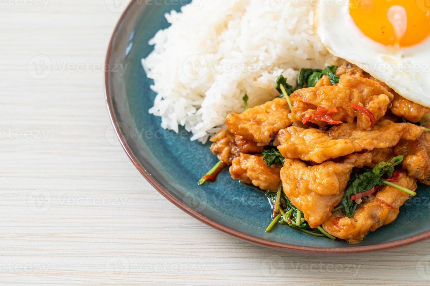 stir-fried fried fish with basil and fried egg topped on rice photo