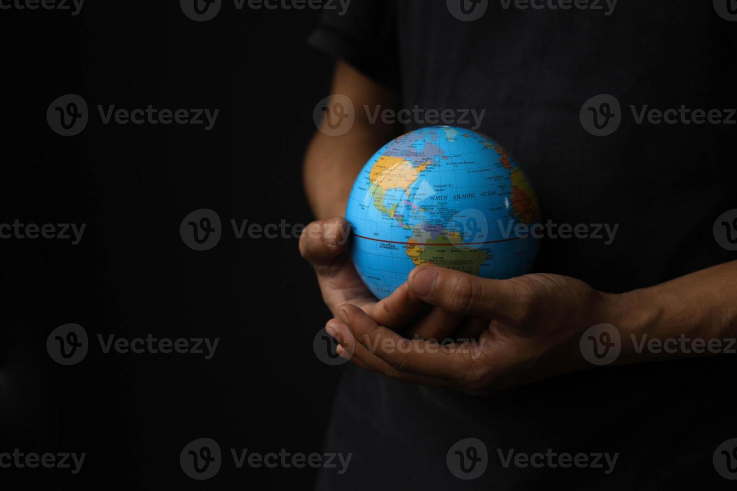 High angle view of hands holding a globe on a black background. Earth day concept with low key tone photo