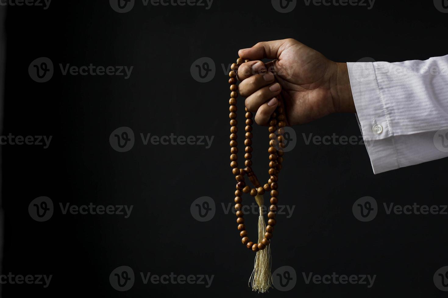 Muslim man hand holding prayer beads isolated on black background with copy space photo