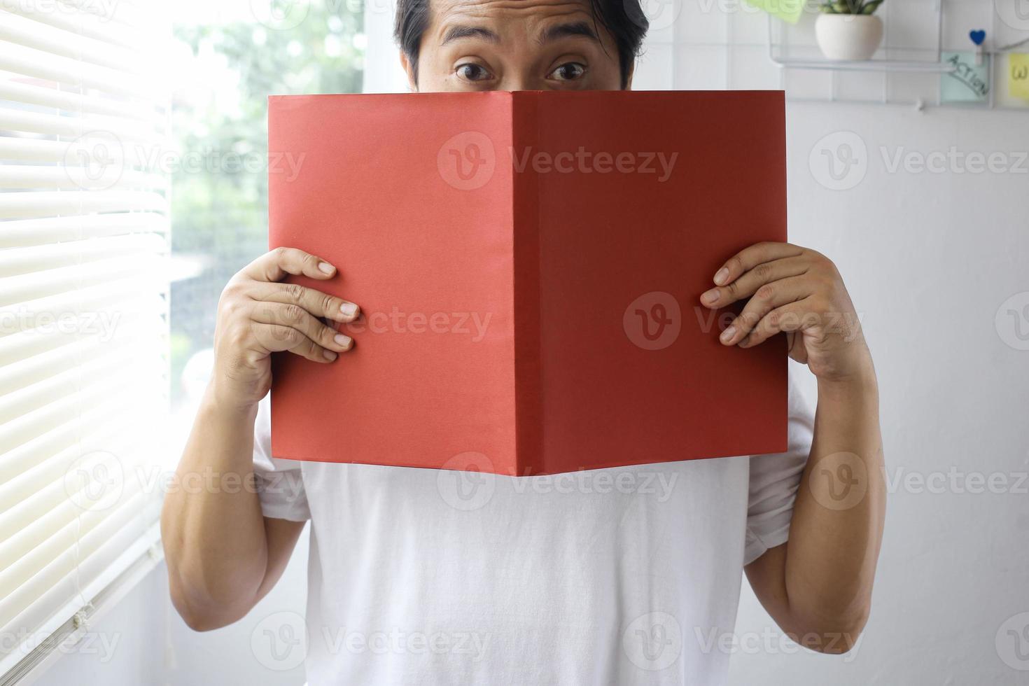 Man peeking and covering his face from behind red book for book mock up photo