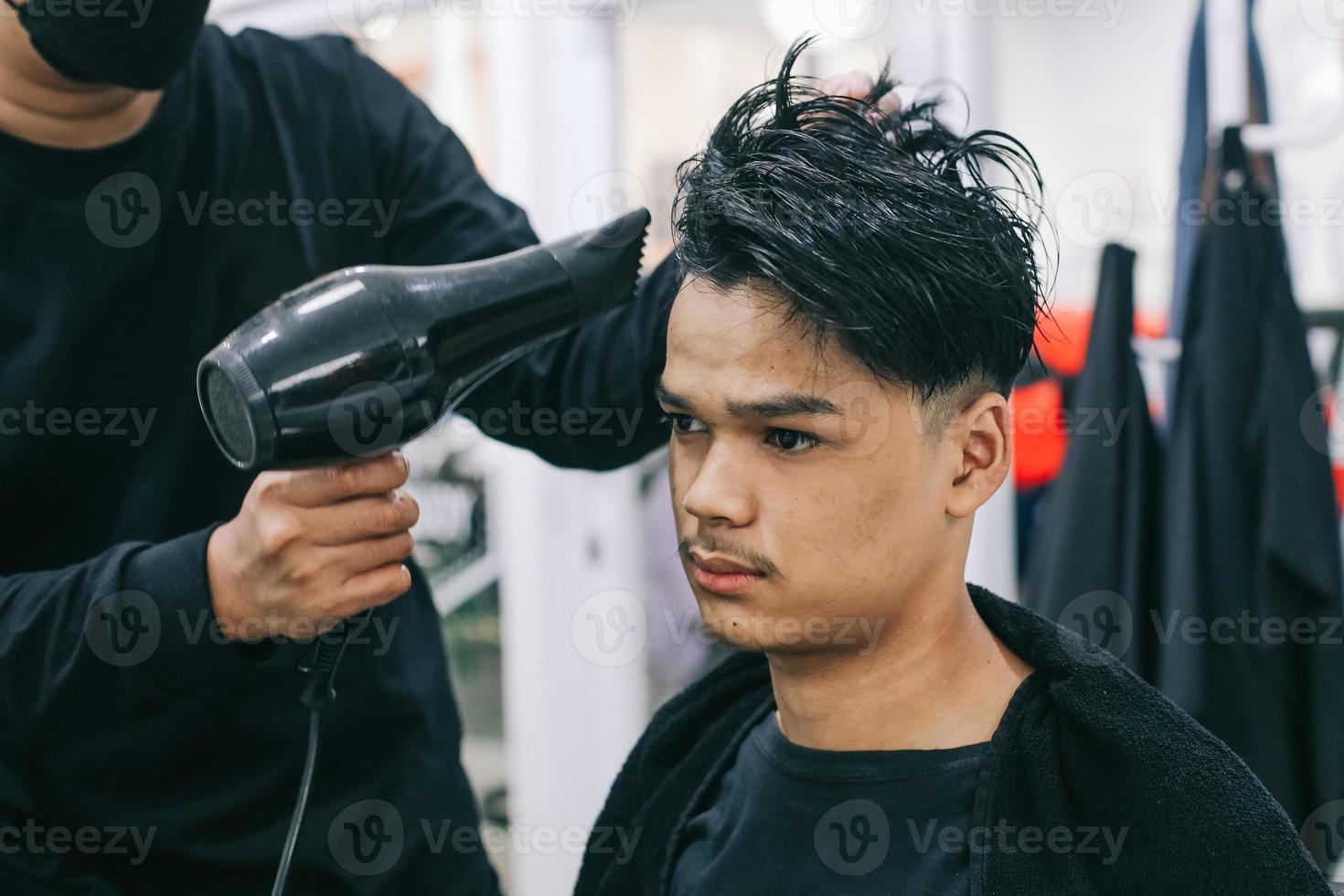 joven visitando la barbería. peluquero secando el cabello del consumidor. autocuidado, belleza masculina. Barbero. peinado moderno foto