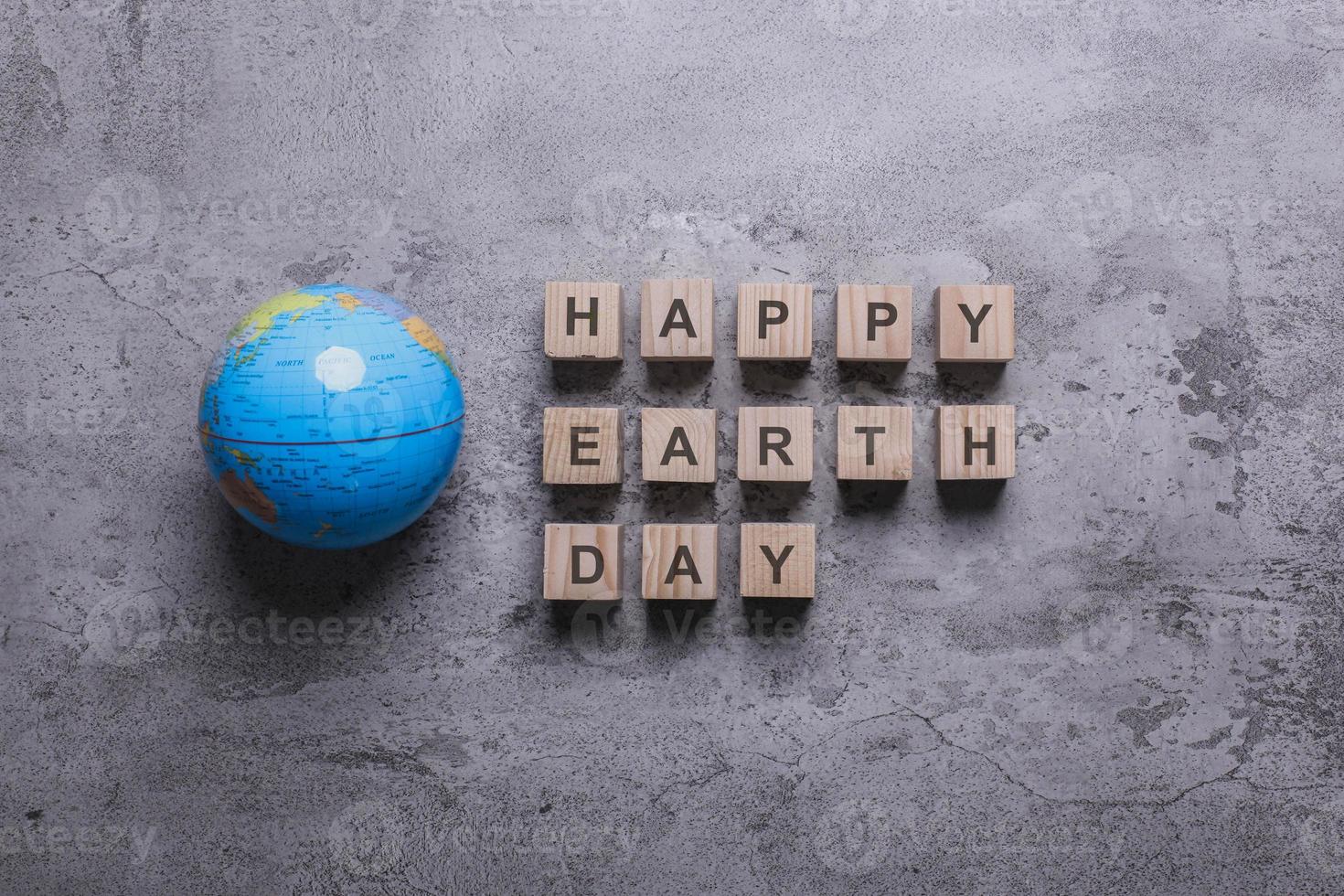 Flat lay composition of globe with happy earth day quotes on wooden cube on cement texture background photo