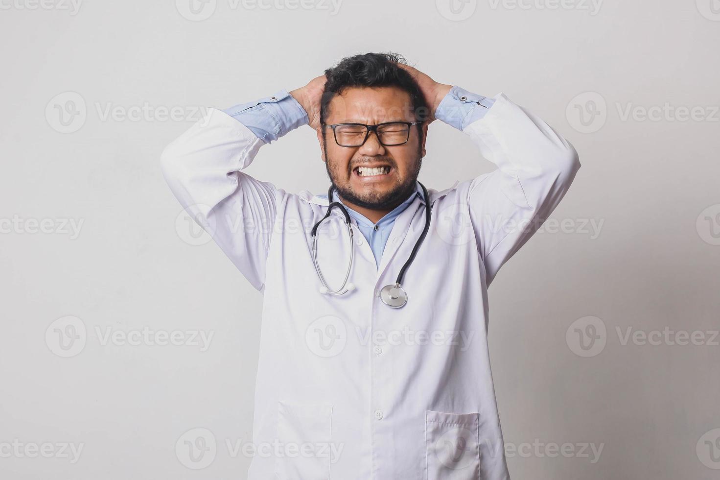 médico varón con expresión frustrada sosteniendo la cabeza con ambas manos aislado sobre fondo blanco foto