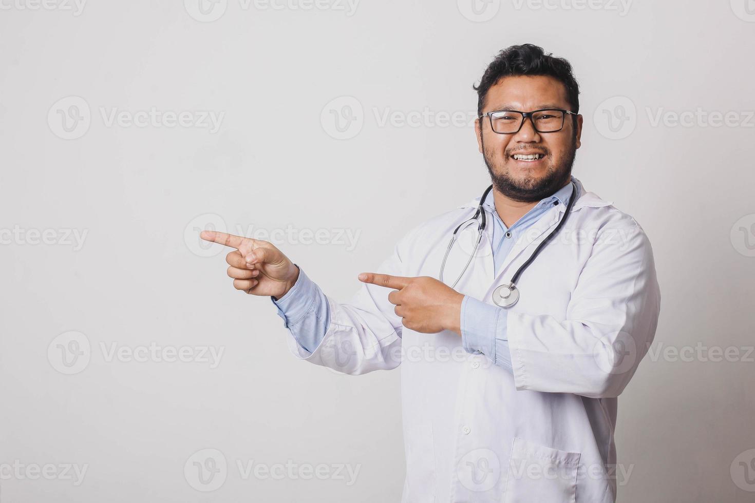 Cheerful male doctor with sideways pointing gesture at copy space isolated on white background photo