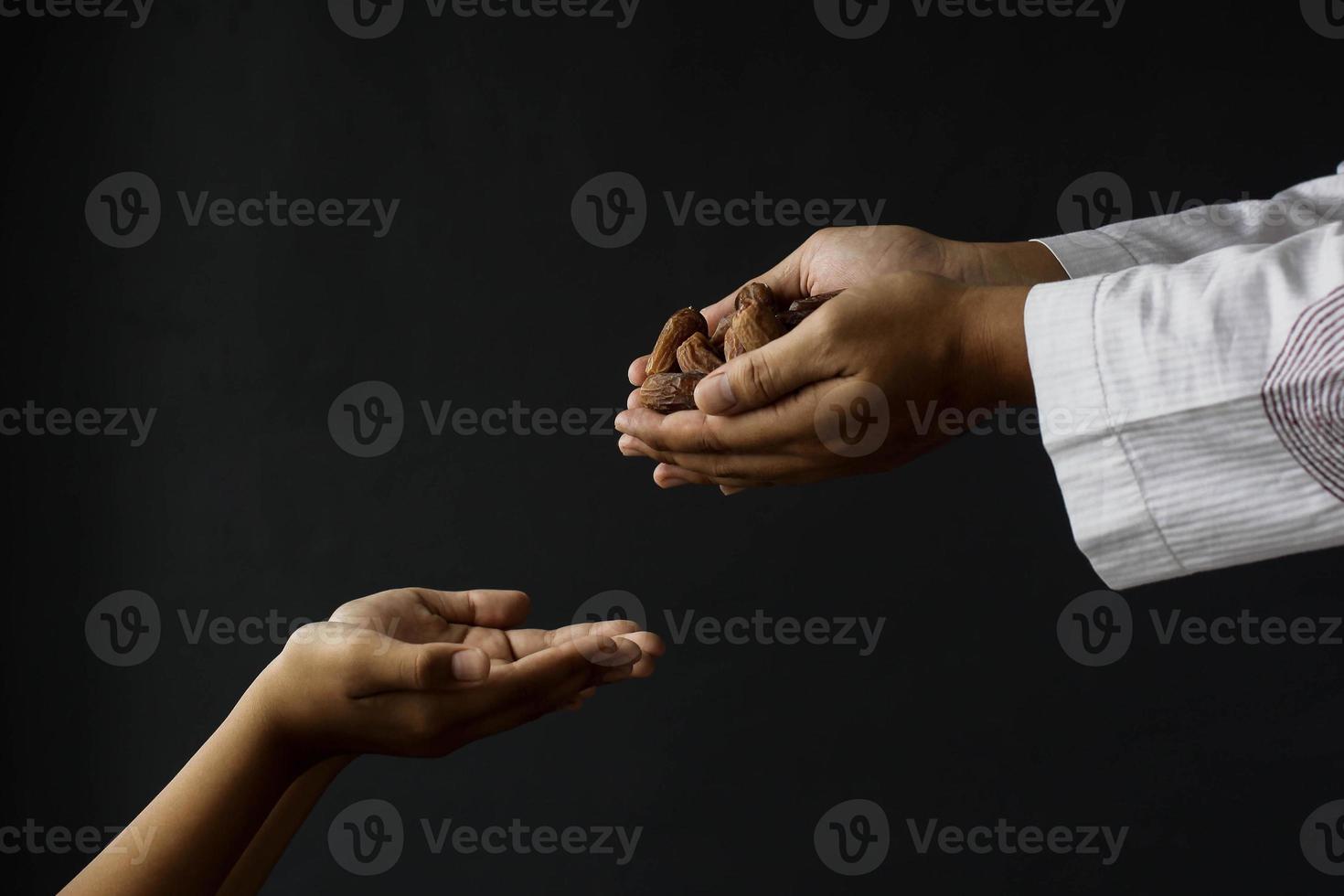 concepto de ramadán kareem. vista lateral manos musulmanas dando la mano llena de fechas aisladas sobre fondo negro foto