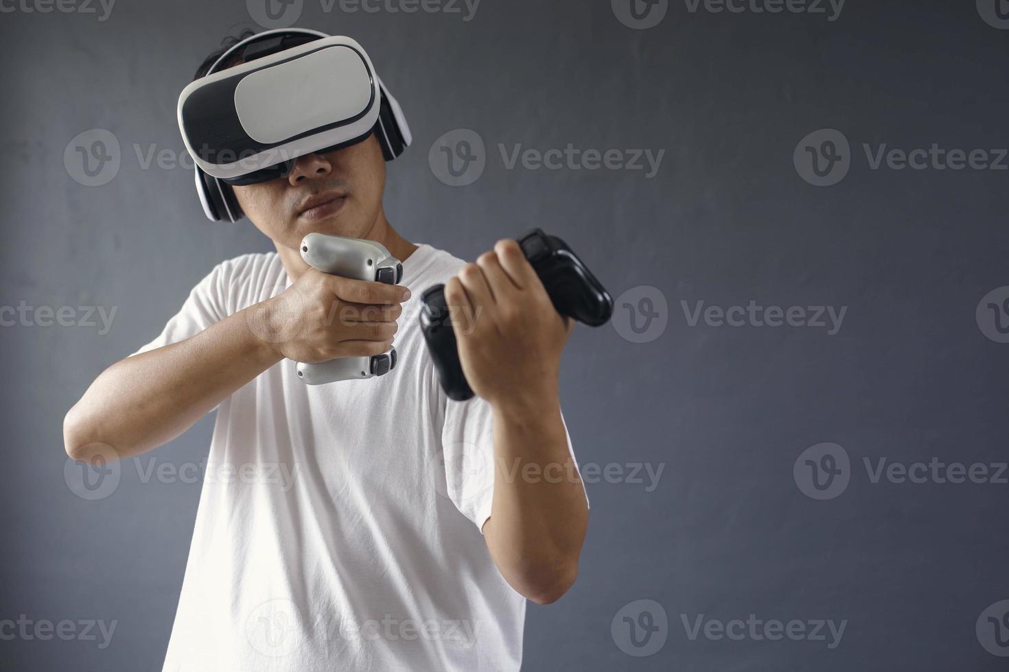 Asian man seriously playing games using VR googles and consoles againts dark grey background. Copy space for games production concept. photo