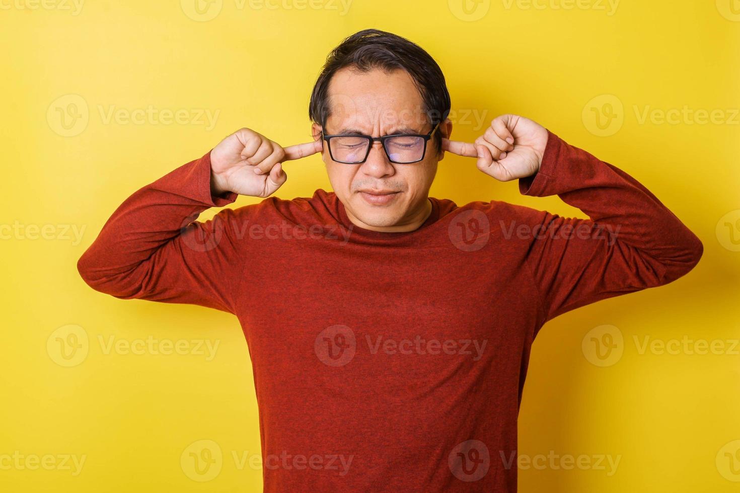 Casual man in glasses covering ears with fingers isolated on yellow background. Annoyed Expression photo