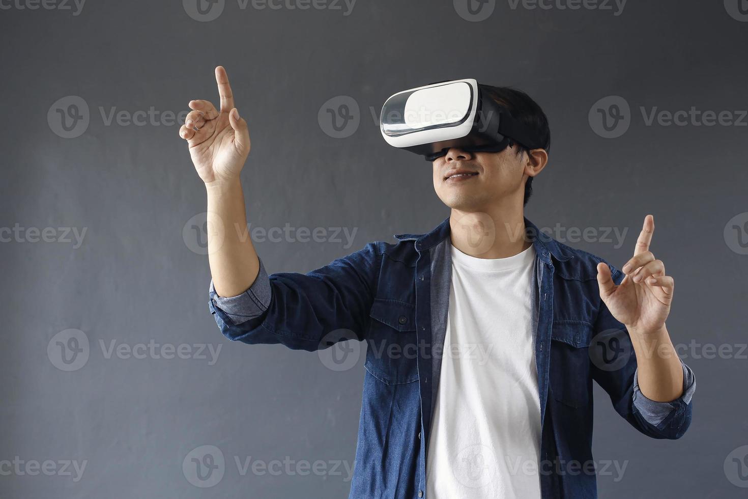 Young man using virtual reality goggles, his hands is touching or clicking isolated on dark grey background. Copy space for futuristic business, education and games concept. photo