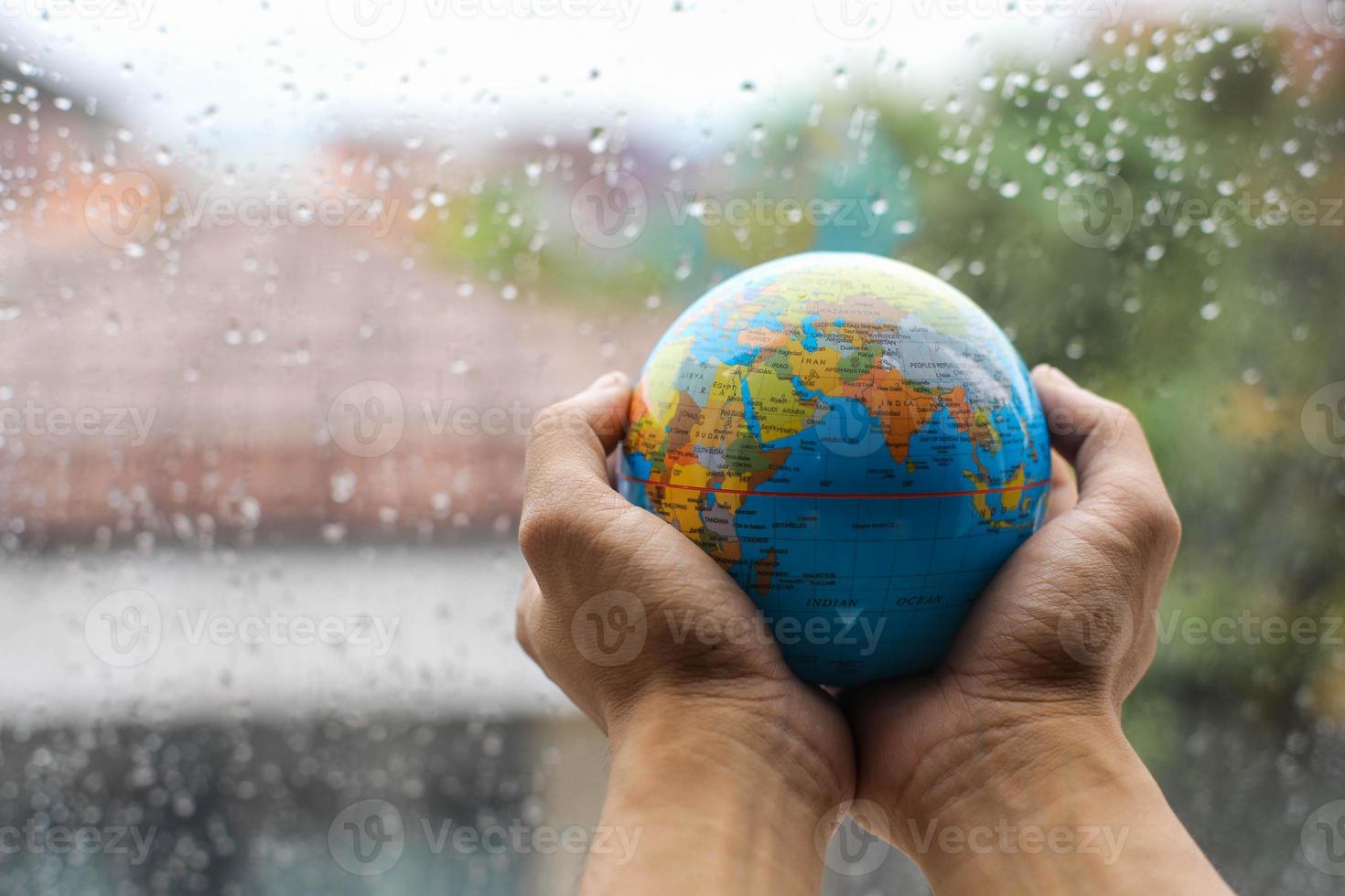 Hands holding globe on blurred rain background. Earth day concept photo