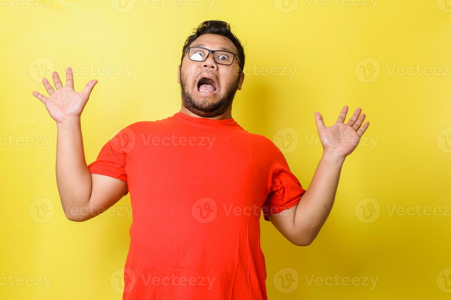 Fat asian guy with shocked, scared expression raising his hands isolated on yellow background photo