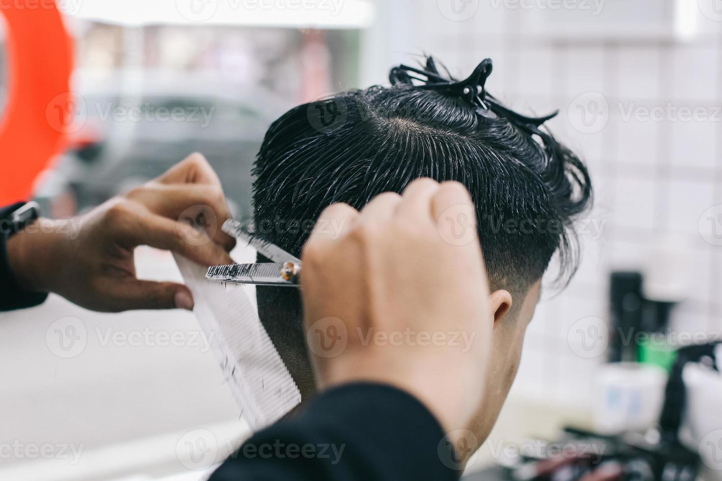 vista posterior de las manos peluquero afeitando el cabello del consumidor con tijeras para adelgazar el cabello foto