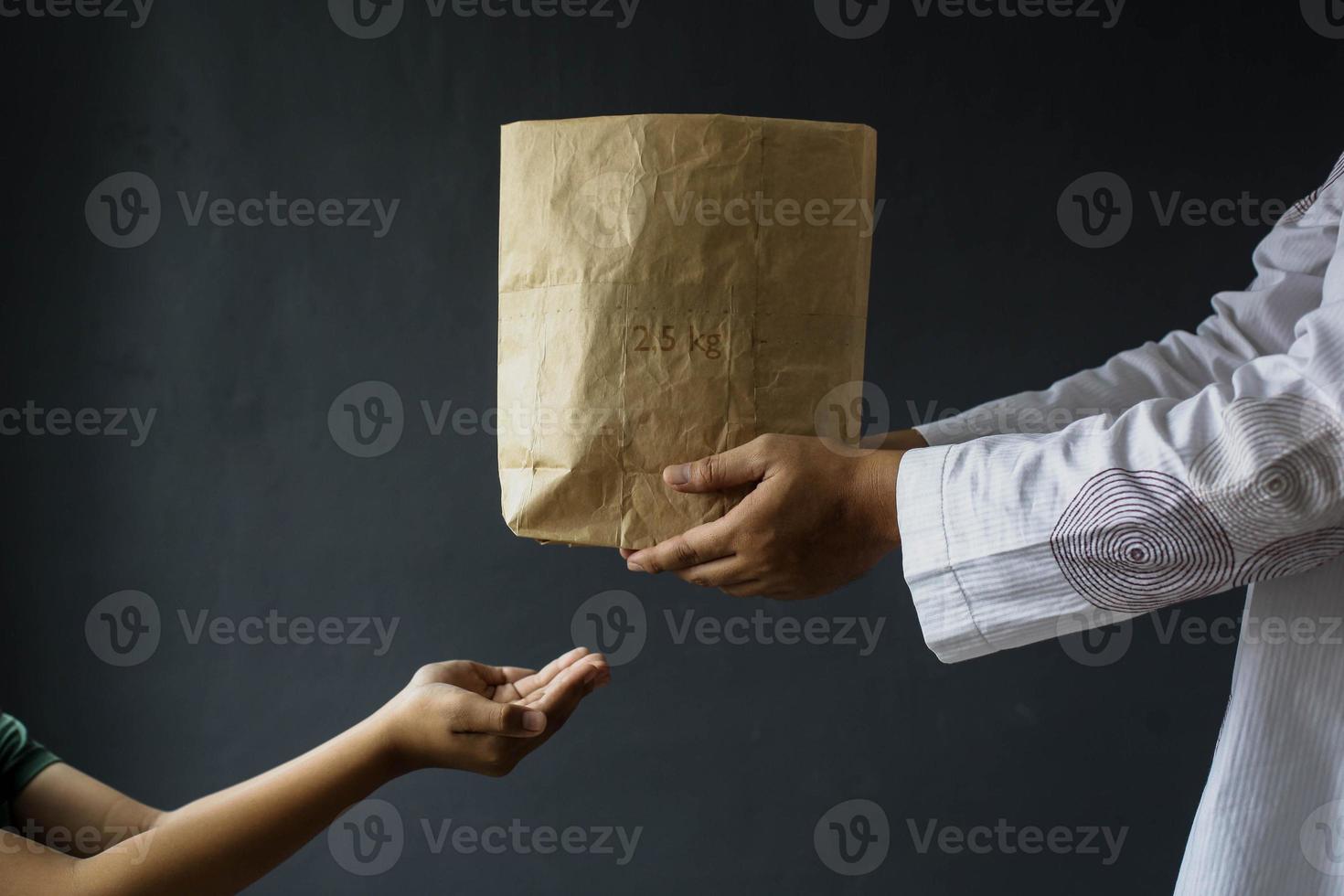 vista lateral de manos musulmanas compartiendo bolsas de limosnas de arroz aisladas en fondo negro. foto