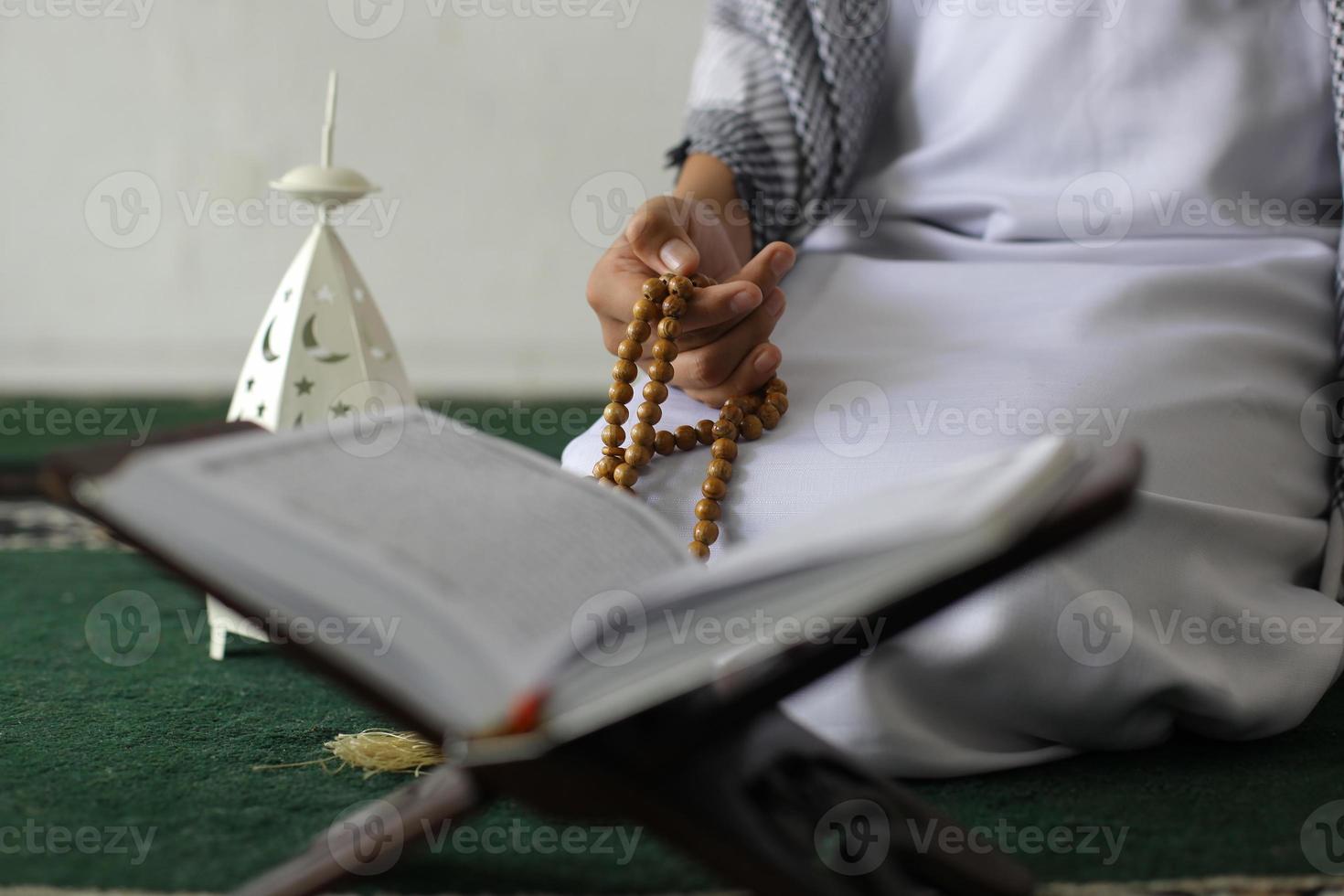 Male hand holding muslim rose beads, prayer beads with quran, over white background photo