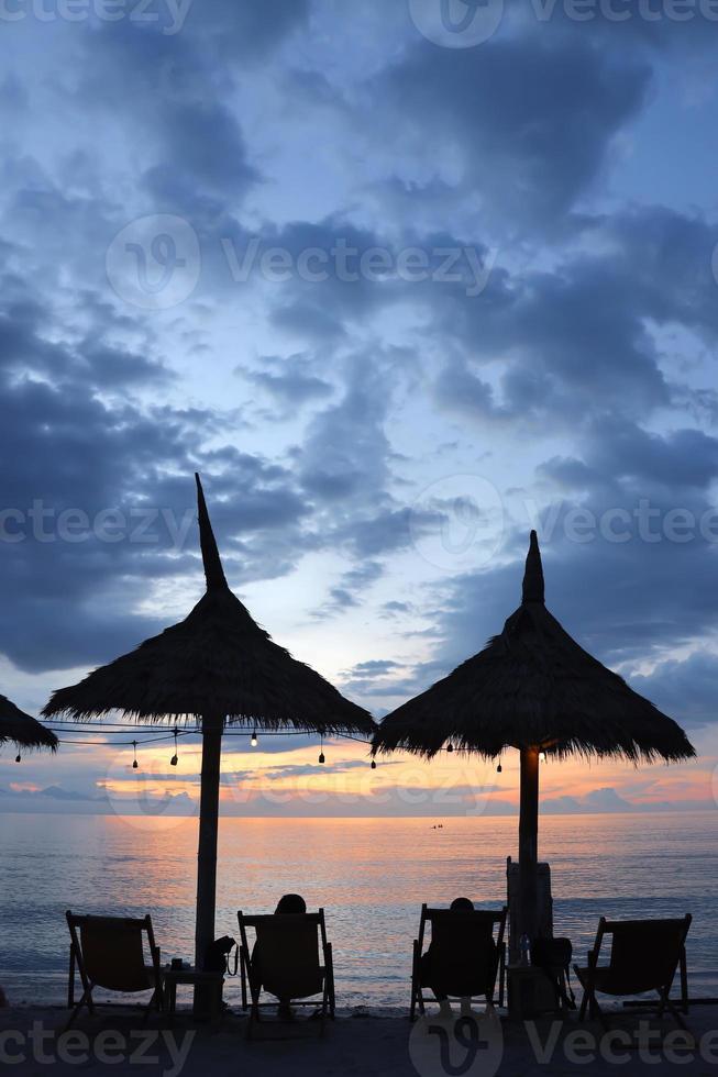 Summertime vacation. Couple are relaxing at lounger beach enjoying sunset time. Copy space for travel and lifestyle concept photo