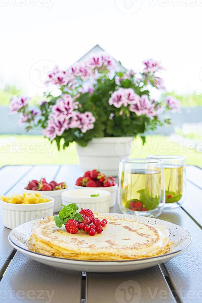 Pancakes with caramelized apples, raspberries, strawberries and red currants. Brunch with green tea and crepes. photo