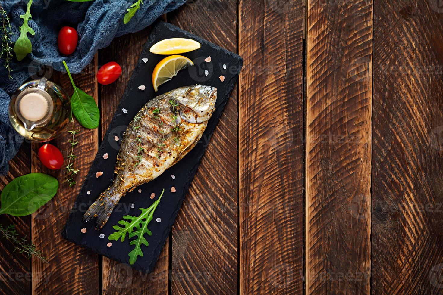 Grilled dorado fish on wooden background. Roasted seafish with spice and herbs photo