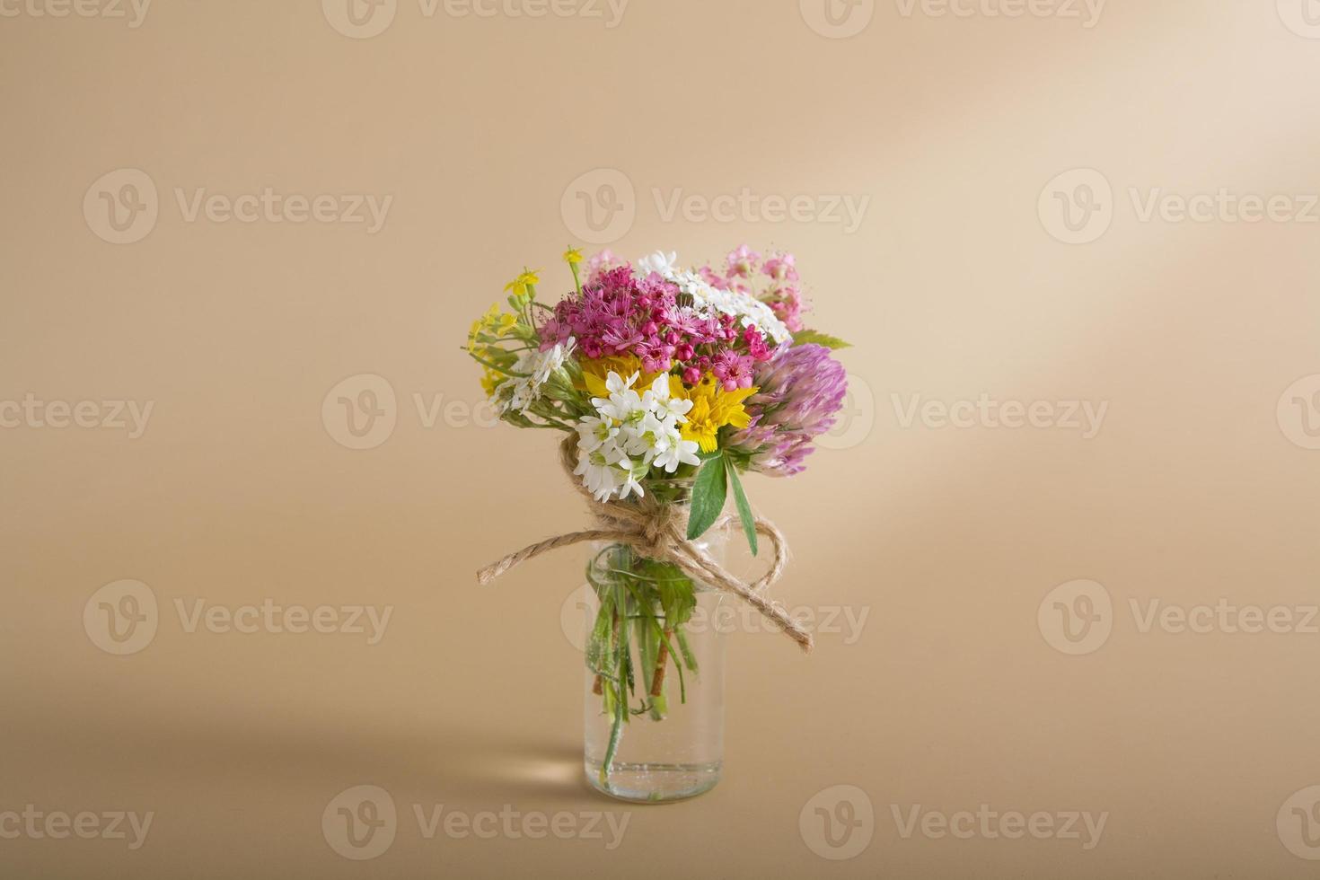 Miniature glass bottle with wildflowers on a beige background for congratulations on March 8, Easter, Mother's Day photo