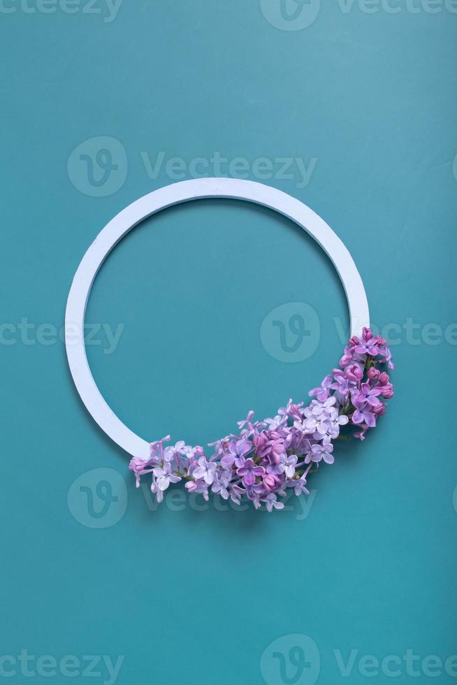 Summer or spring composition on a turquoise background. Lilac flowers with round wooden frame copy space top view. Summer, spring floral concept photo