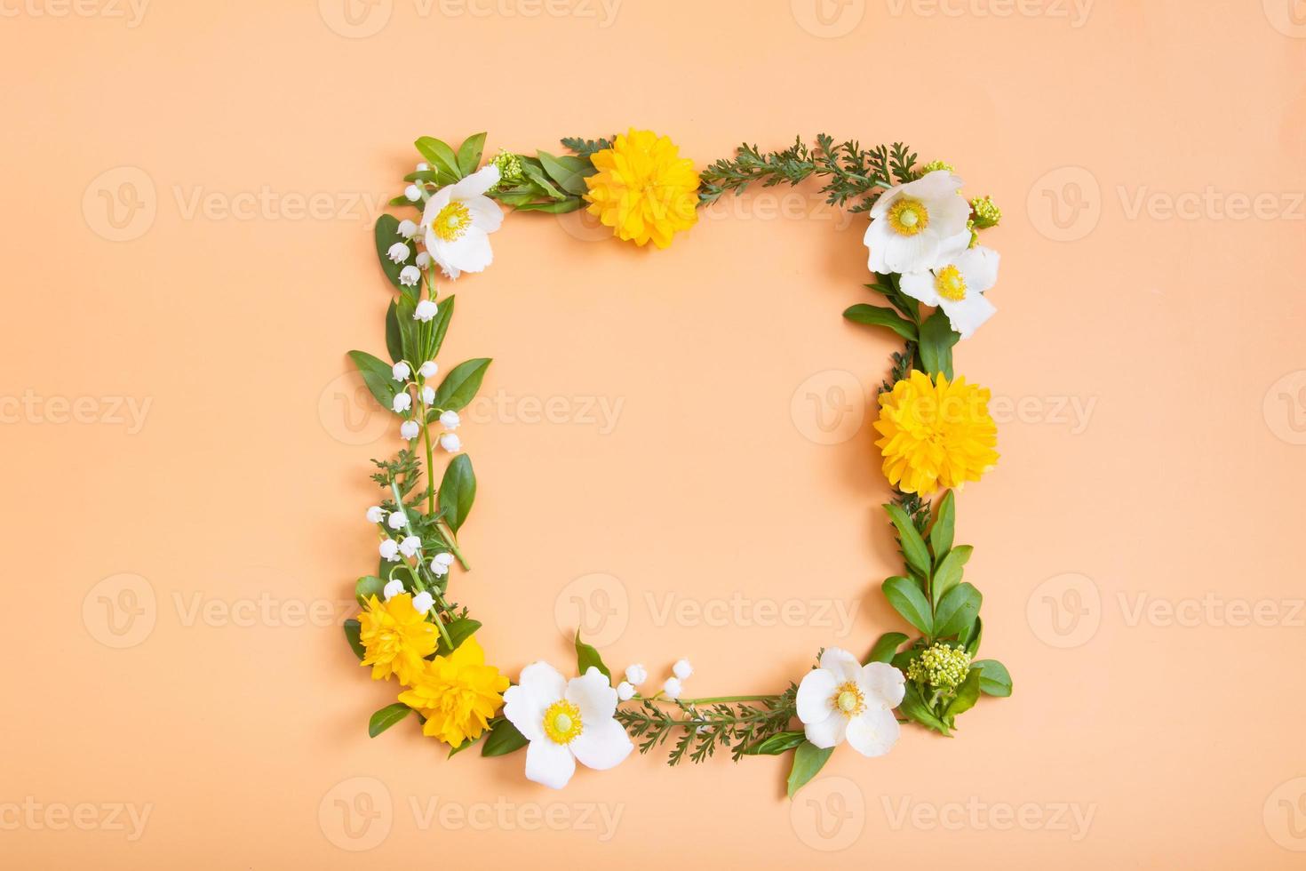 Summer or spring composition on a orangr background. Yellow and white flowers and green leaves with a copy space wreath top view. Summer, spring floral concept photo