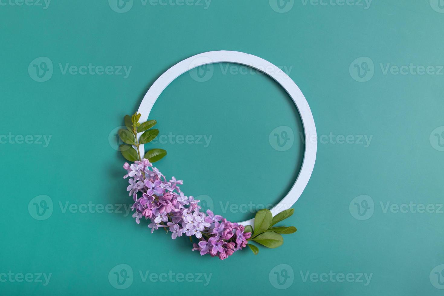 Summer or spring composition on a green background. Lilac flowers with round wooden frame copy space top view. Summer, spring floral concept photo