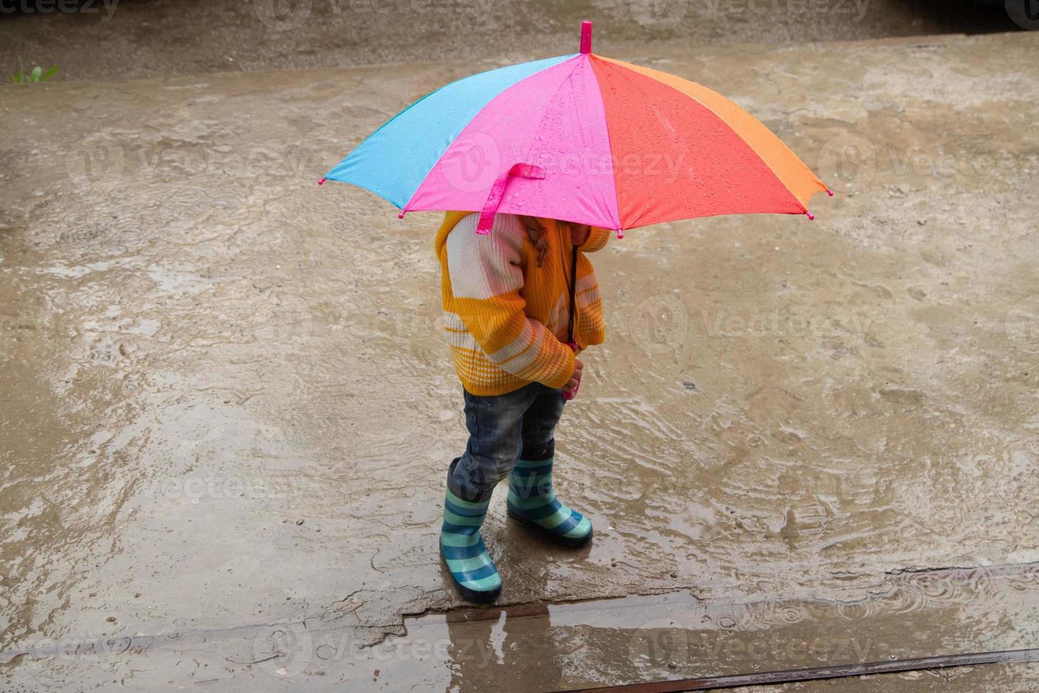 A 3-year-old girl hides in the rain under a colored umbrella photo