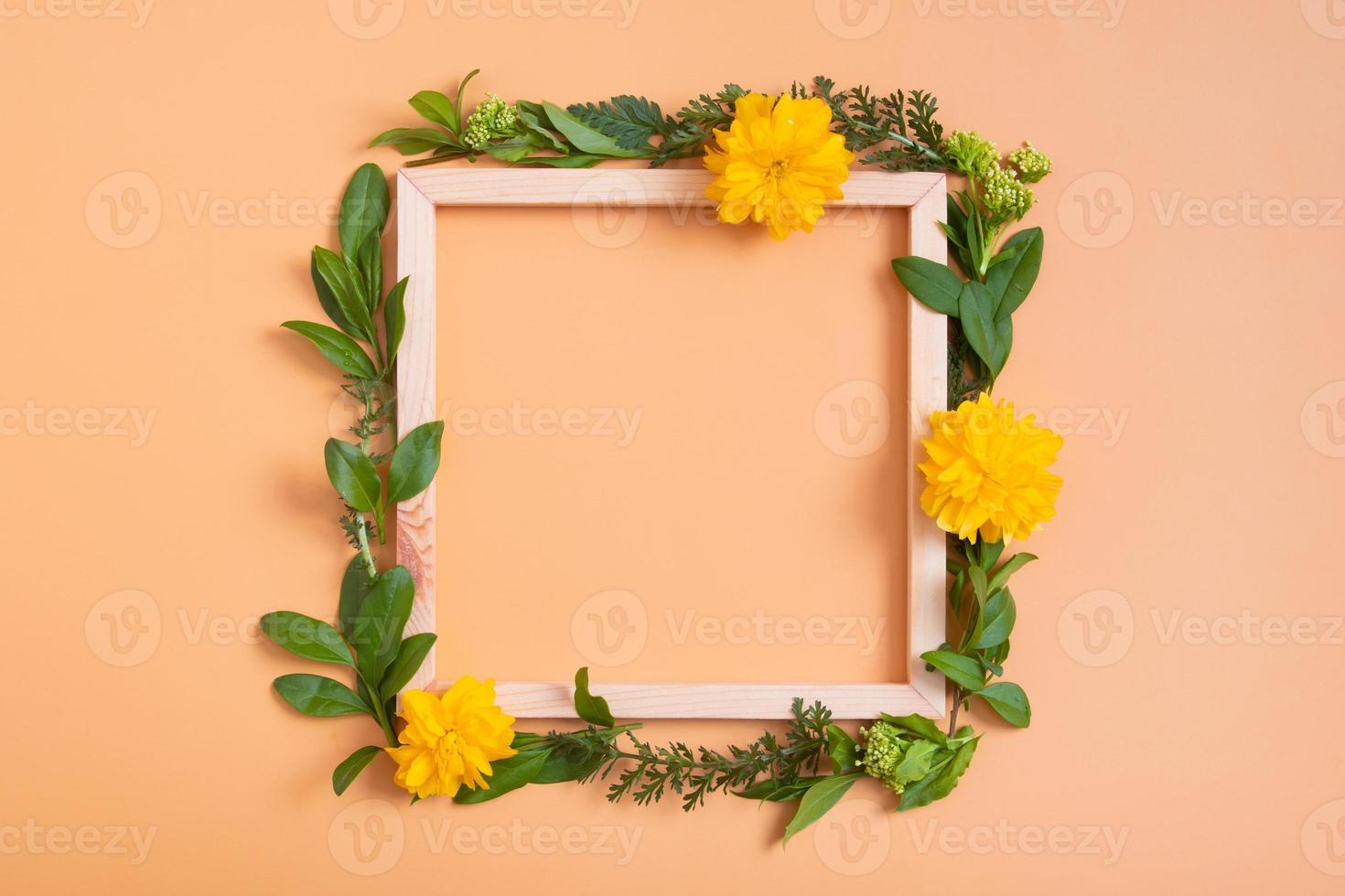 Summer or spring composition on an orange background. Flowers and leaves with square wooden frame copy space top view. Summer, spring floral concept photo