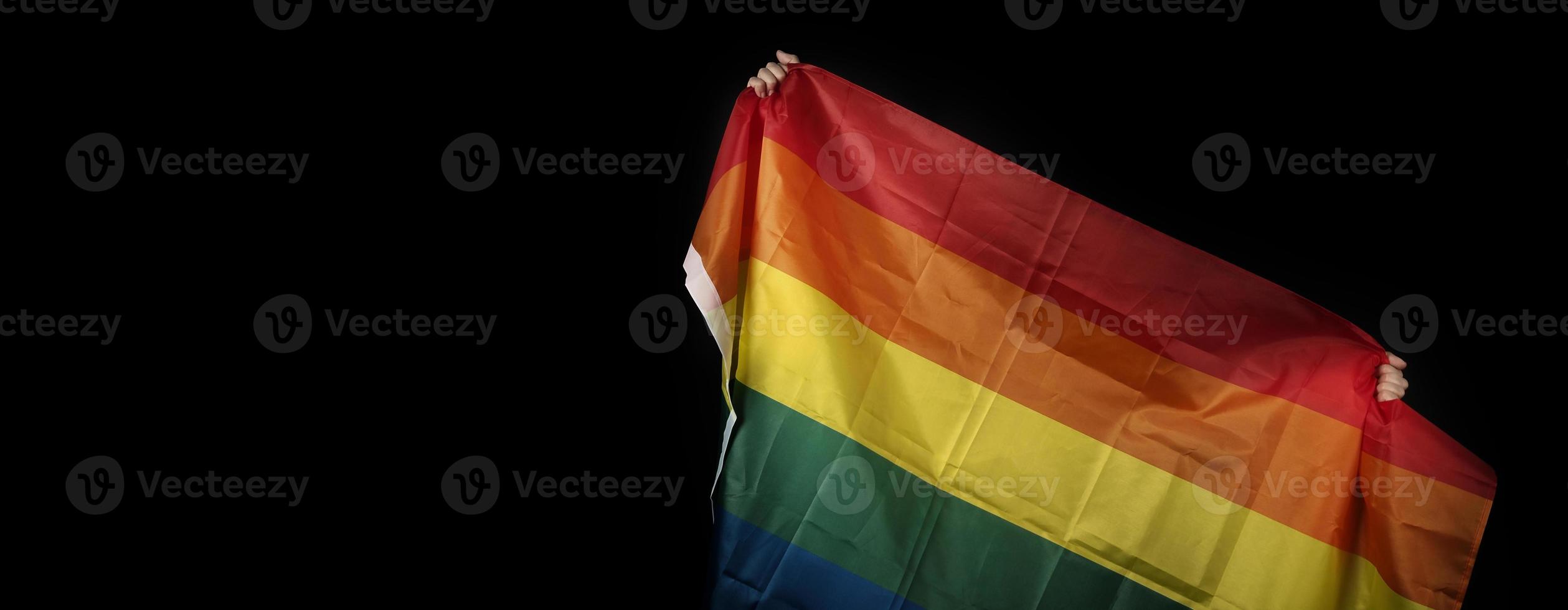 LGBTQ pride flag on black background. Lgbt rainbow flag in gay hand. photo