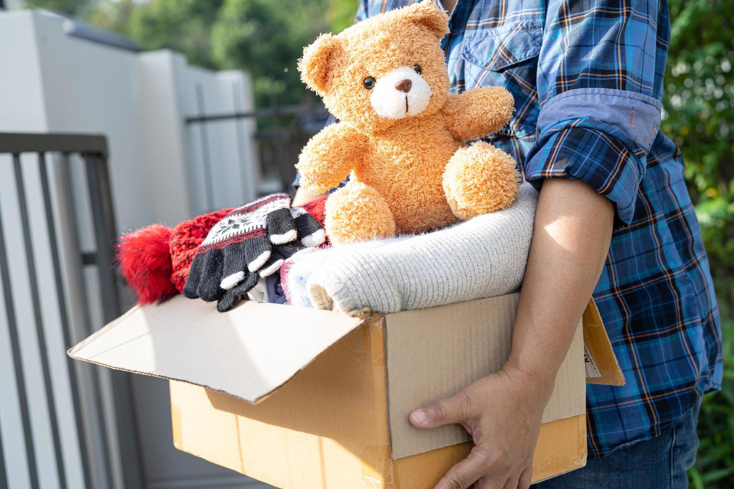 Holding clothing donation box with used clothes and doll at home to support help for poor people in the world. photo