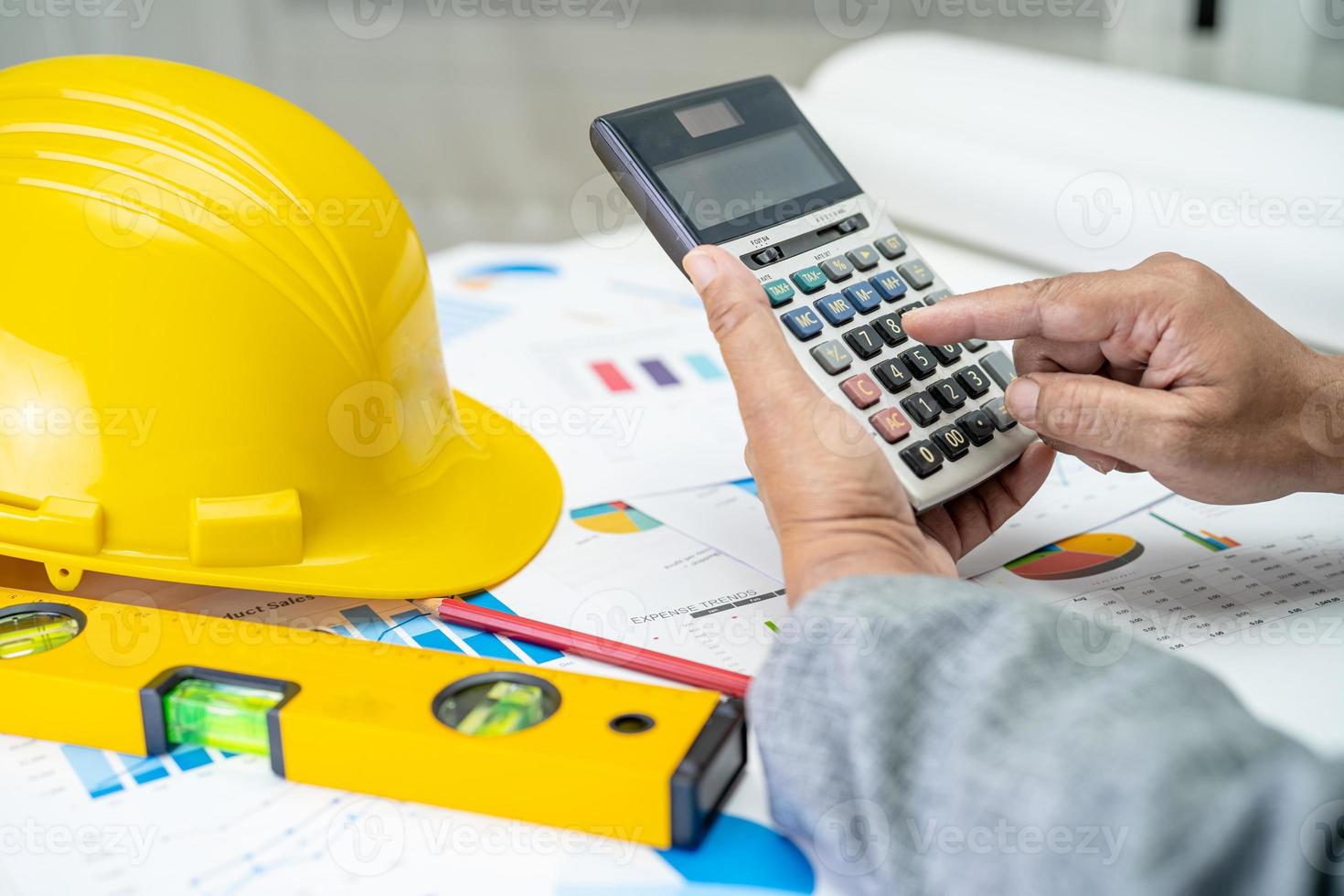 Asian engineer with architectural house plan project blueprint, graph and yellow helmet and engineering construction tools. photo