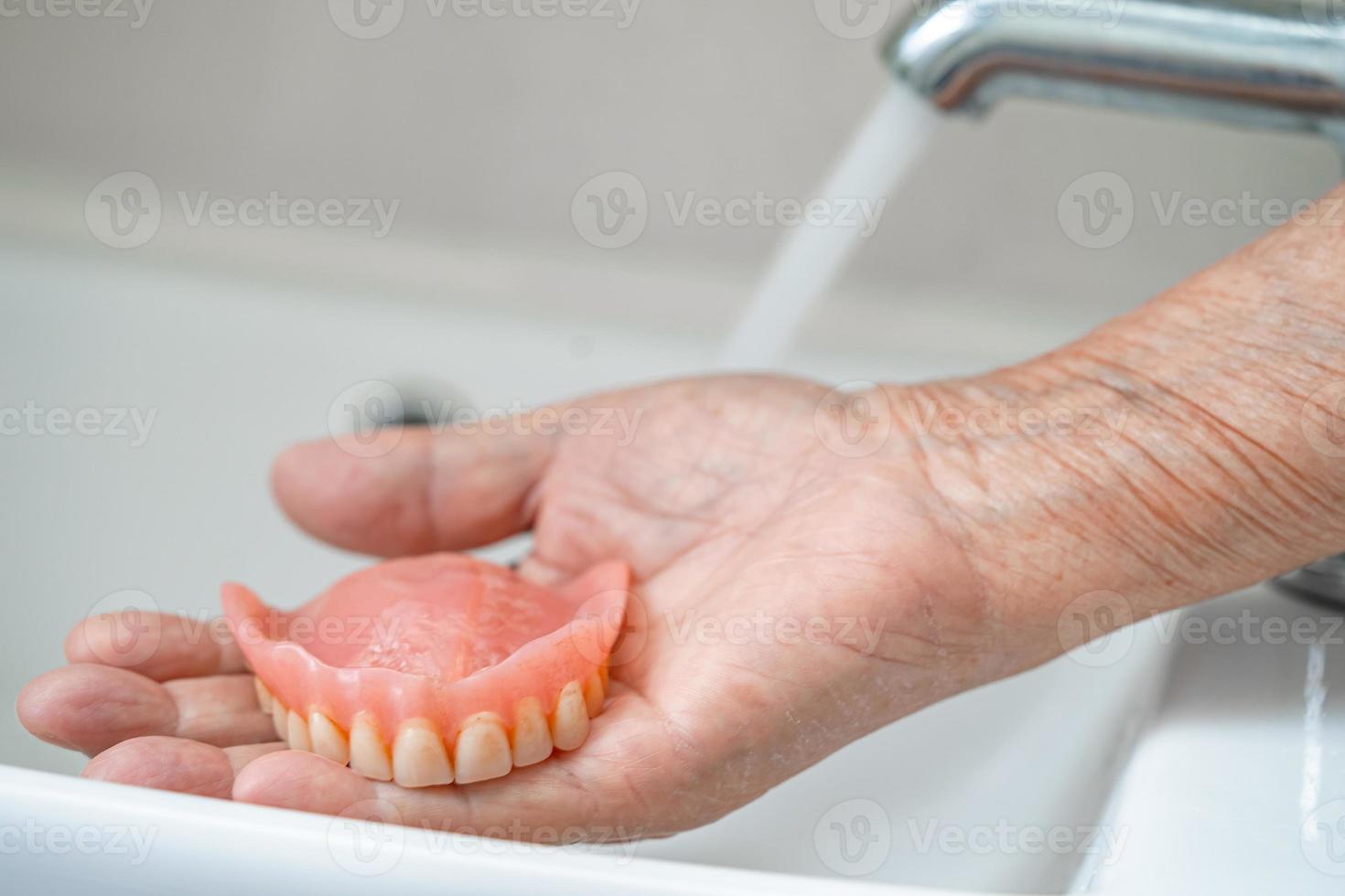 Asian senior or elderly old woman patient holding and washing denture in nursing hospital ward photo