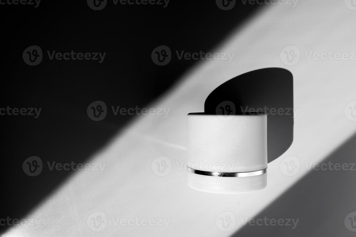 Concept of skincare. Closeup of a white plastic jar with moisturizing body or face cream in direct sunlight on a white background. photo