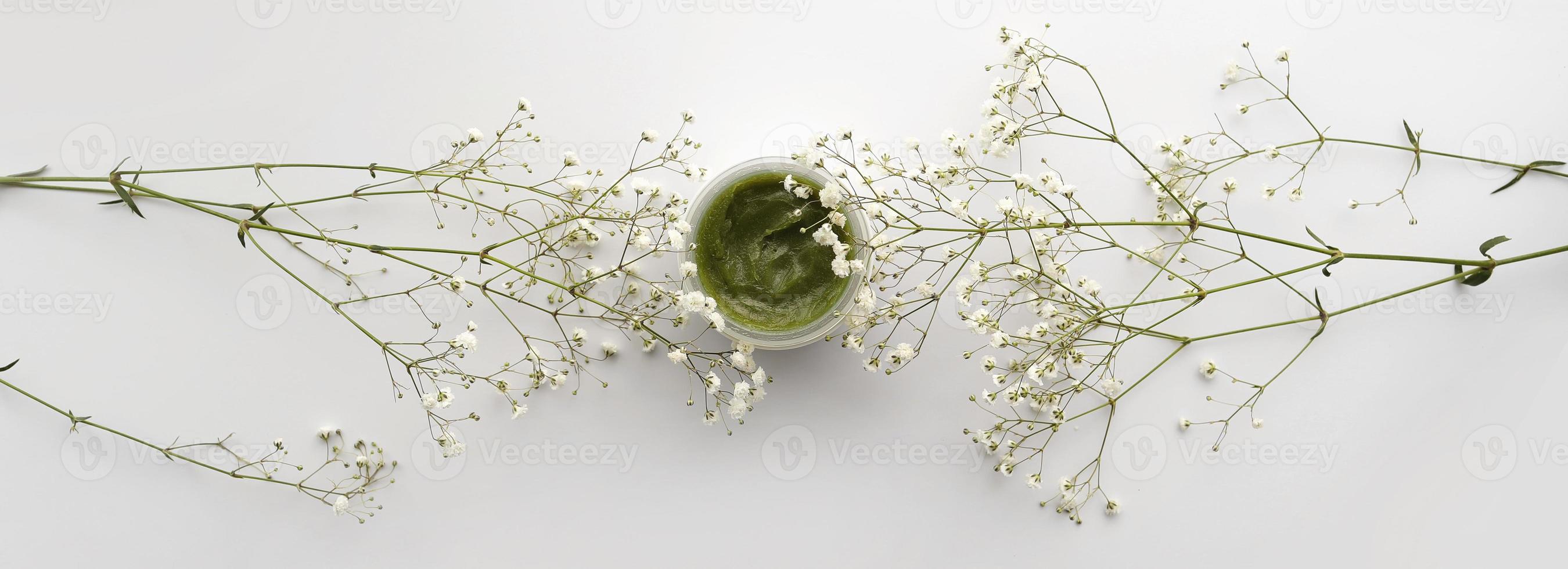 baner of organic face cream in container and white flowers on white background. Home made remedy and beauty product concept. Top view. Copy space. photo