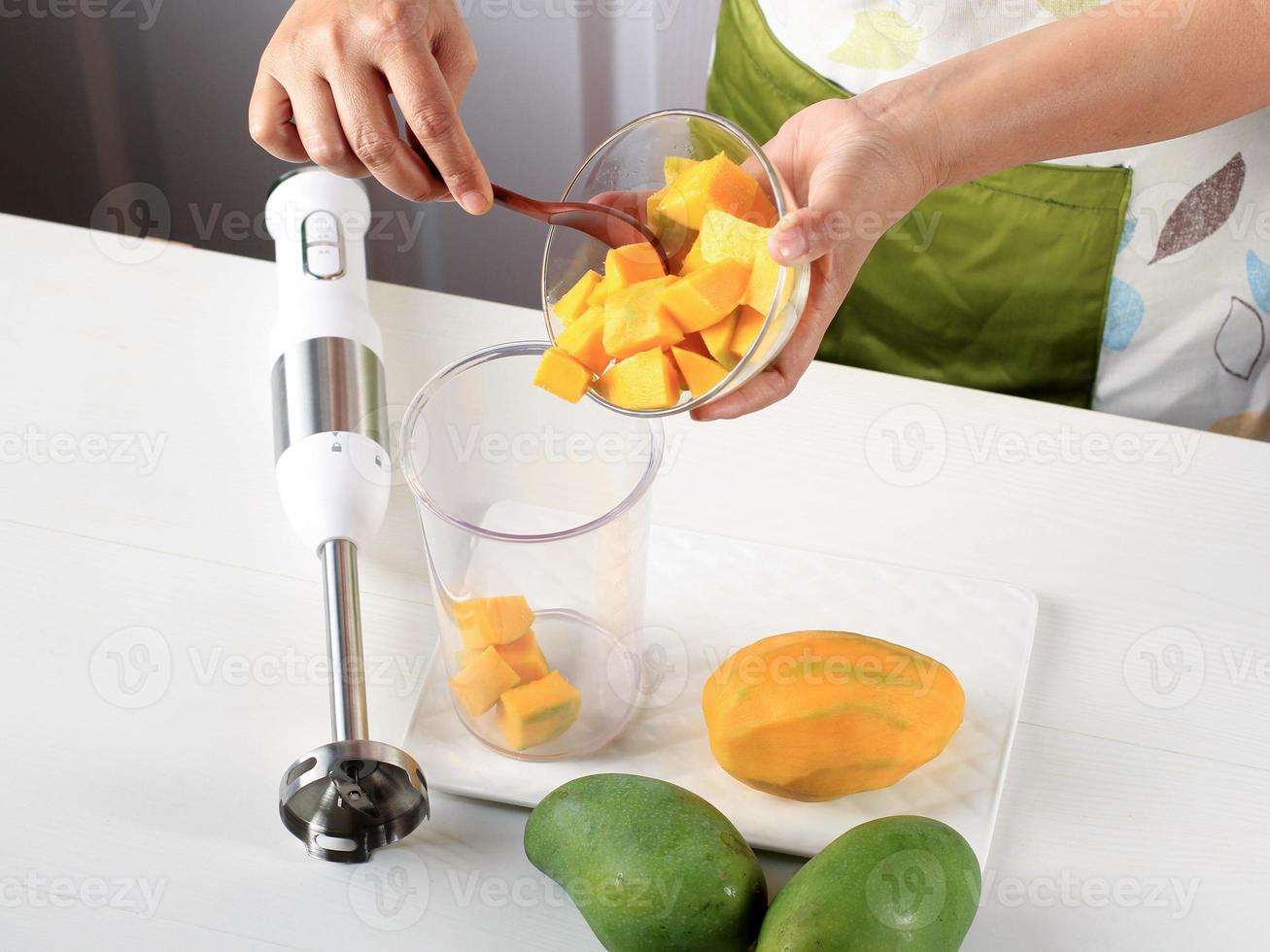 Female Chef hand Pour Diced Mango to the Juicer Bowl, Process Making Mango Smoothie or Mango Lassi in the Kitchen photo