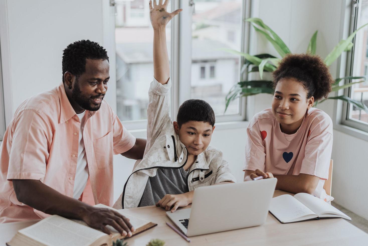 niño asiático aprendiendo clases en línea desde casa con su familia. el niño pequeño se sienta con su hermana y su padre usando una computadora portátil aprendiendo educación en línea desde casa. foto