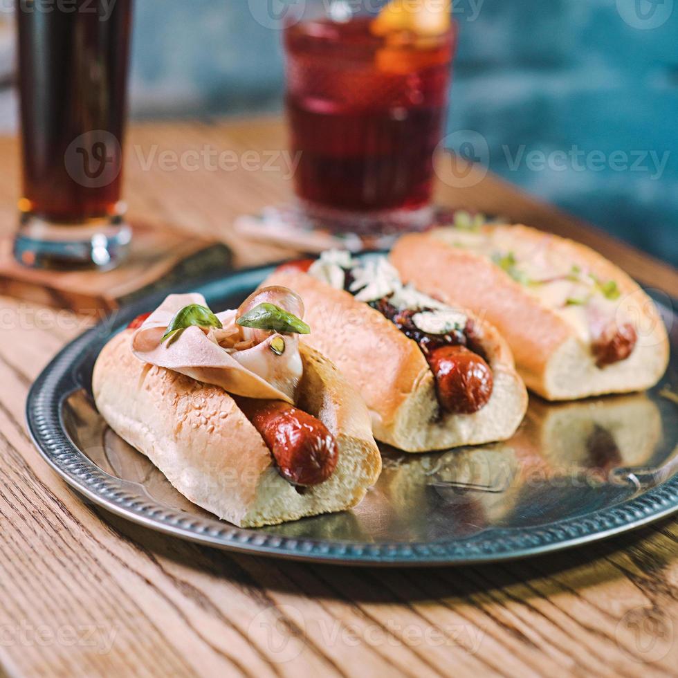 hot dogs with sausages, ham and vegetables, alcohol cocktail oldfashioned and beer on the table in the bar photo