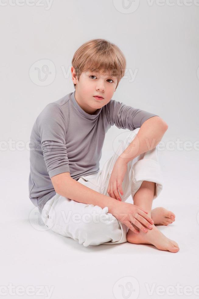 Portrait of cool young stylish boy sitting on the floor, light background photo