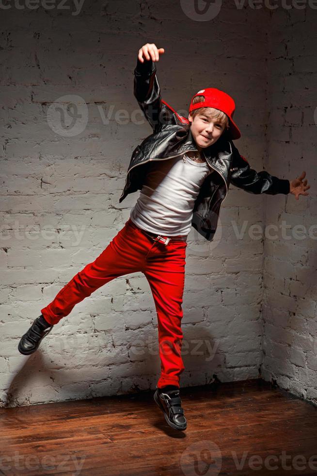 retrato de un joven y genial hip hop con sombrero rojo y pantalones rojos y camisa blanca y chaqueta de cuero negro en el desván foto