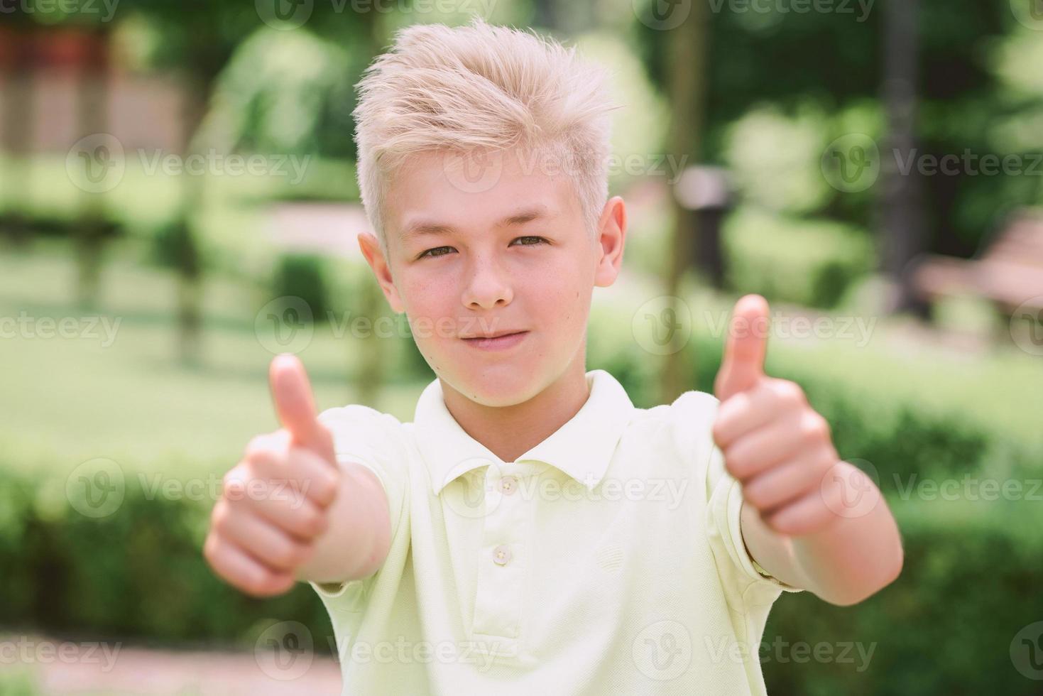 portrait of cute handsome blonde eleven old boy with thumb up outdoor. Good sign and ok concept photo