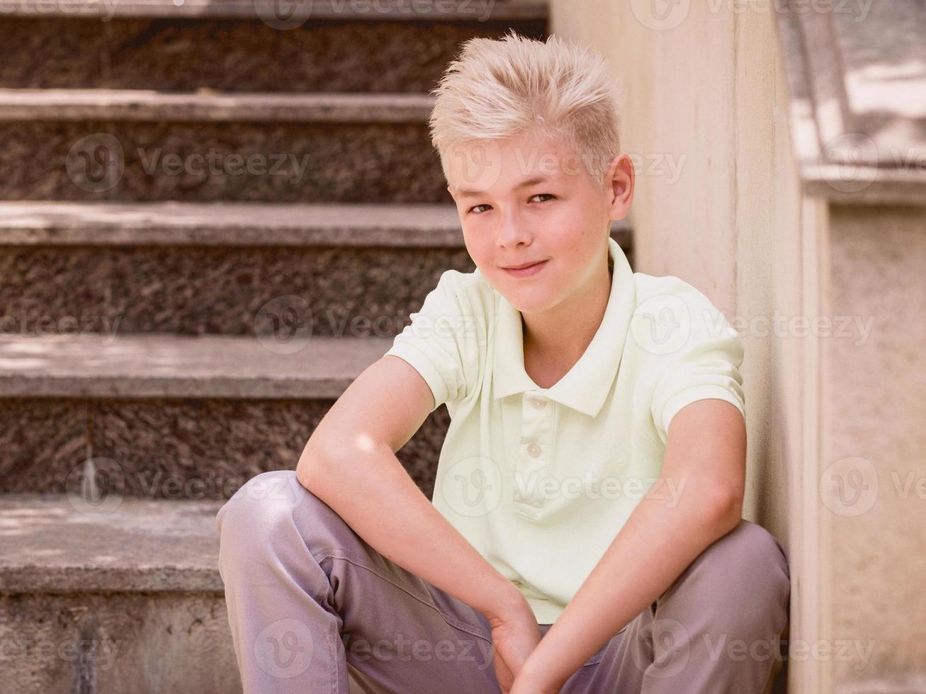 portrait of cute handsome blonde eleven old boy sitting on the stairs outdoor. Growing up, childhood, separating concept photo