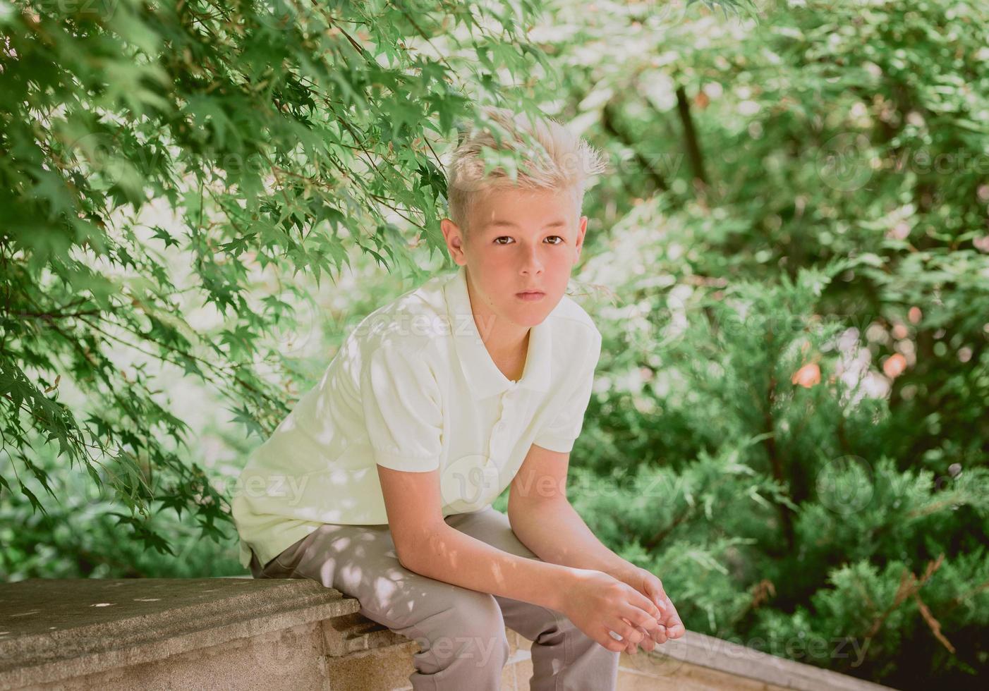 portrait of cute handsome blonde eleven old boy sitting outdoor in the park. Growing up, childhood, separating concept photo