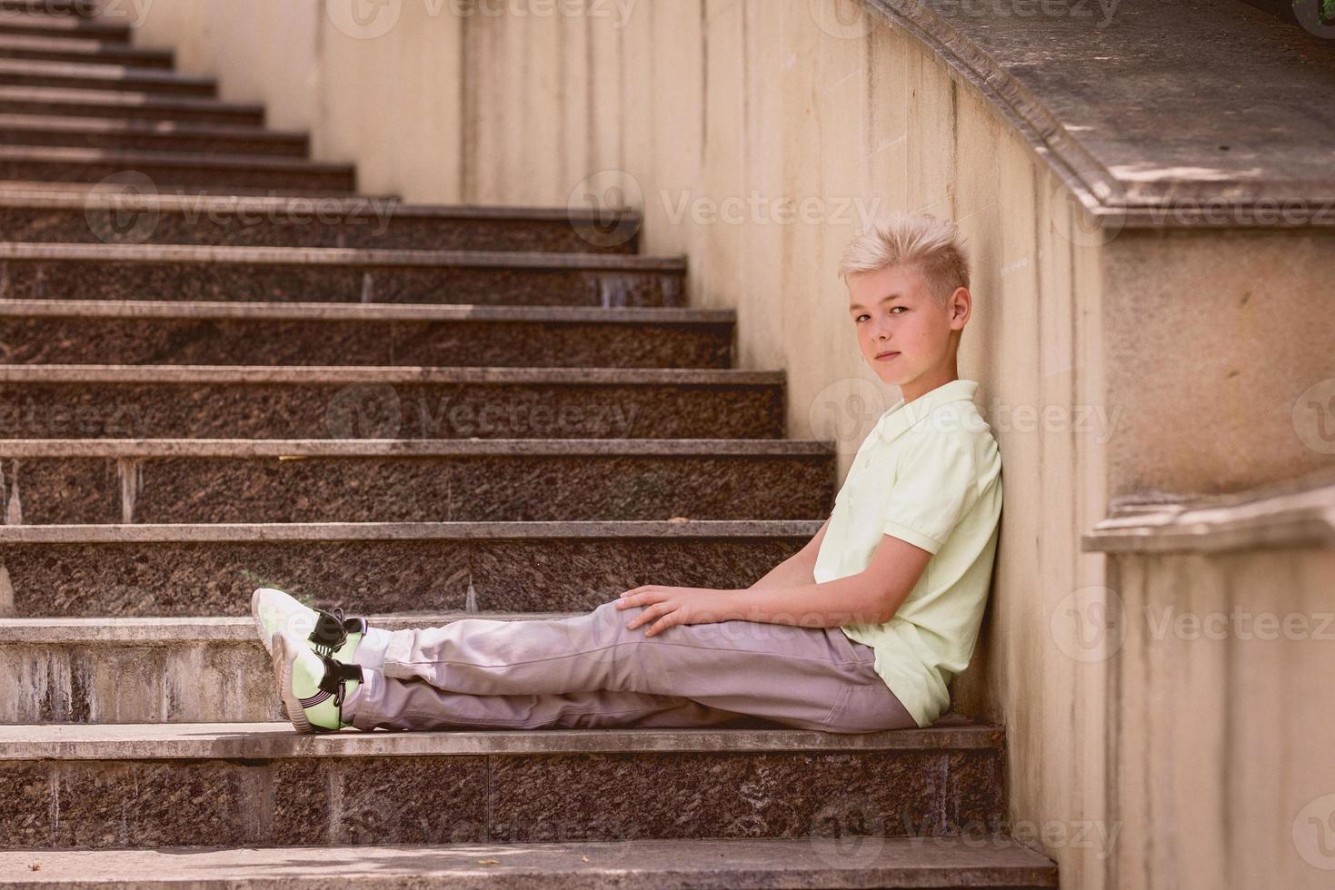 portrait of cute handsome blonde eleven old boy sitting on the stairs outdoor. Growing up, childhood, separating concept photo