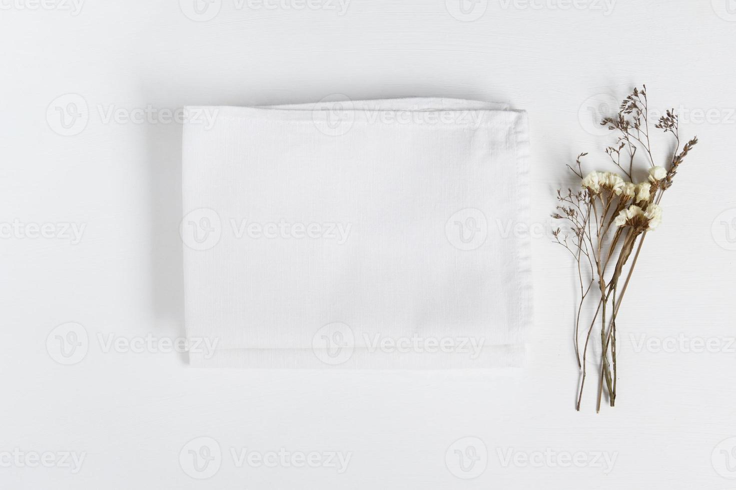 Stack of fabrics with dry flowers over light background. Flat lay with white folded linen cloth for mock up. photo
