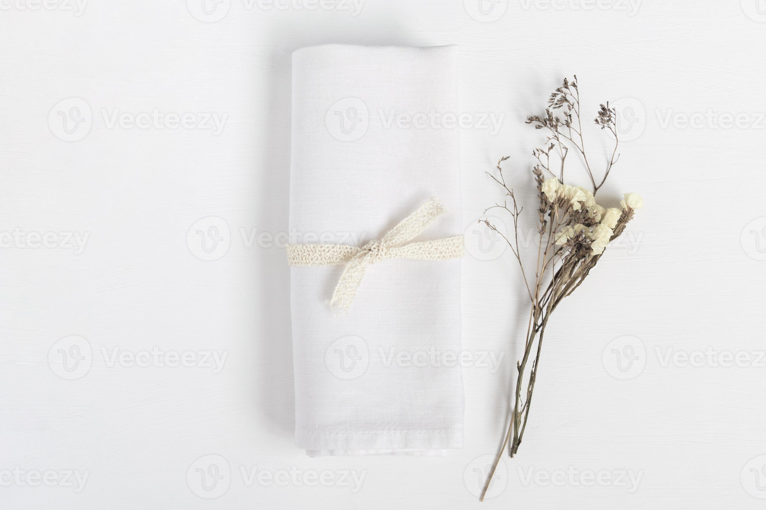 Linen napkin tied with ribbon on white table. Fabric and dried flowers