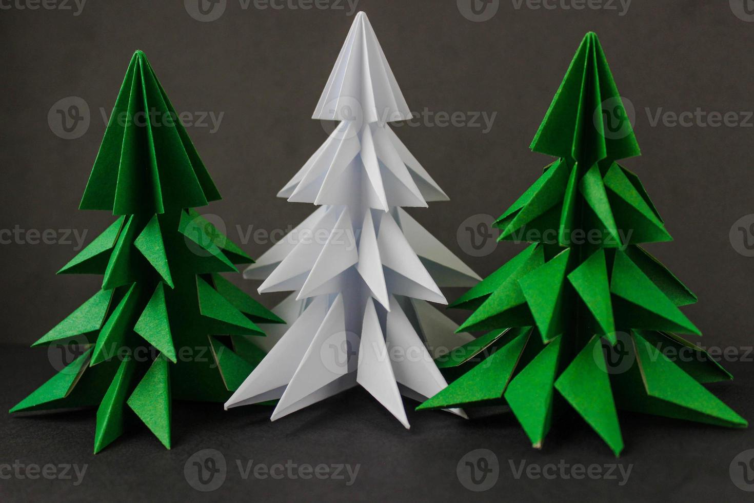 dos árboles de navidad verdes de origami y uno blanco sobre fondo negro. foto