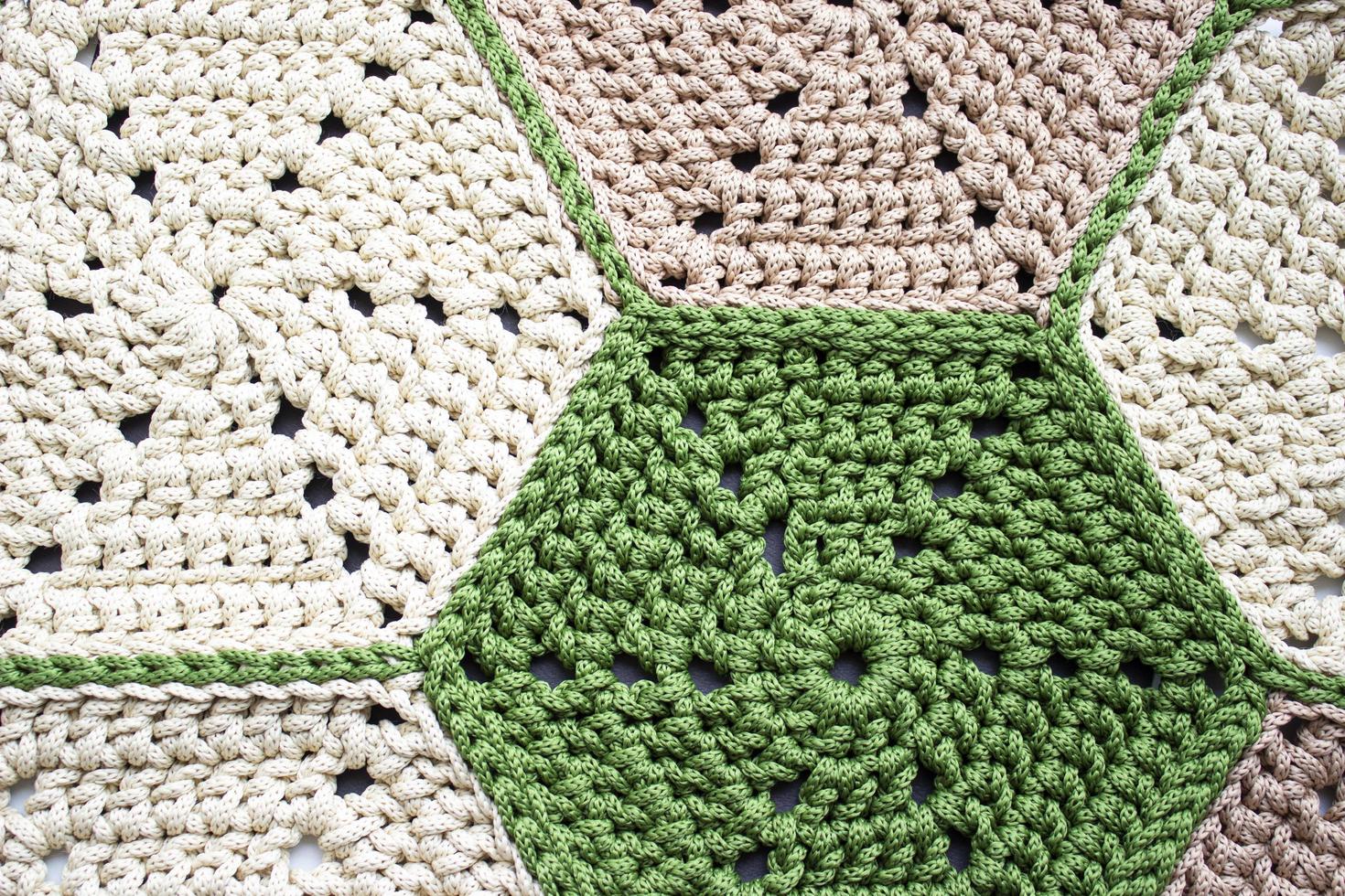 Knitting from a cord. Crocheted carpet of hexagons. Beige and green. Knitting texture. photo